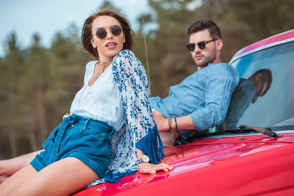 Stilvolles Junges Paar Mit Sonnenbrille Sitzt Auf Rotem Auto — kostenloses Stockfoto