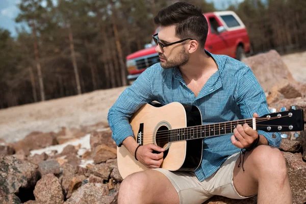 Młody Mężczyzna Gra Gitara Akustyczna Zewnątrz Czerwony Jeep Tle — Darmowe zdjęcie stockowe