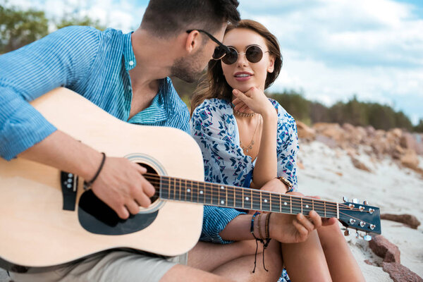 male guitarist playing acoustic guitar and sitting with girlfriend outdoors