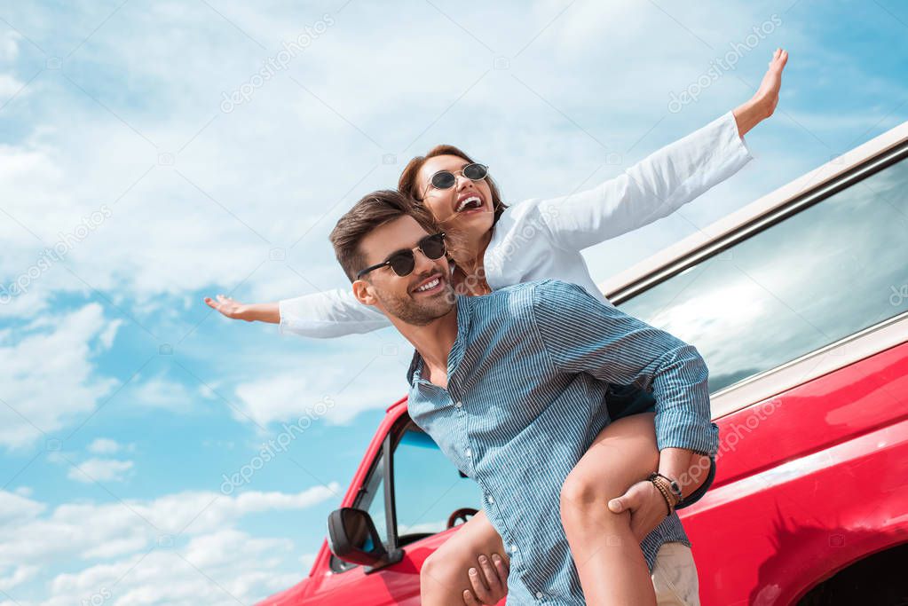 excited young couple of travelers piggybacking at car
