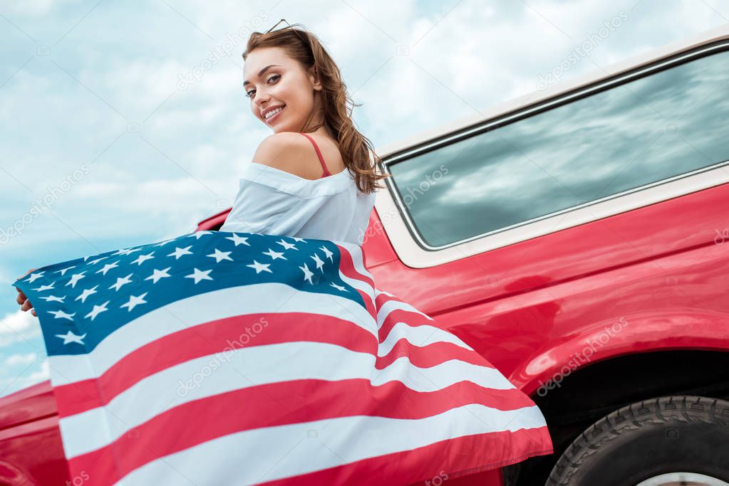 attractive girl with american flag standing near red car