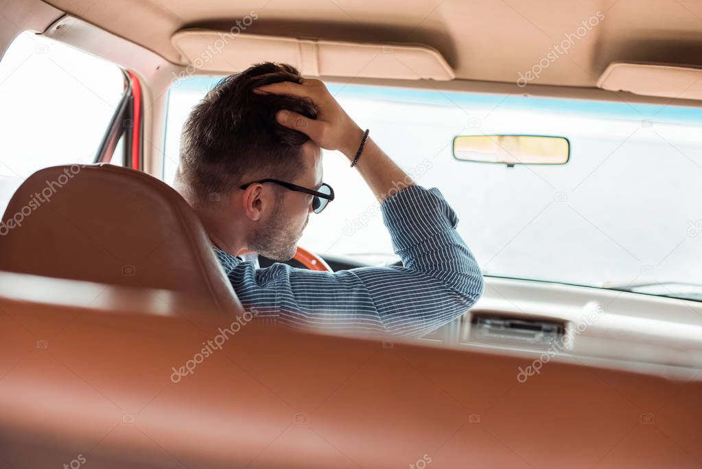 rear view of stylish man in sunglasses driving car during road trip