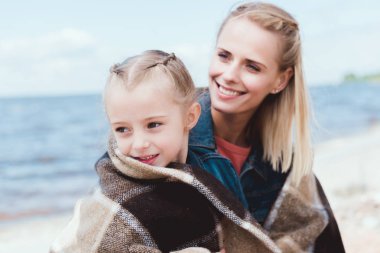 mutlu anne ve kızı deniz kıyısında battaniyeye sarılmış