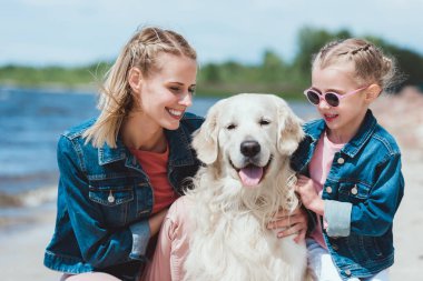 çekici anne ve gülümseyen kızı ile golden retriever köpek deniz kıyısında