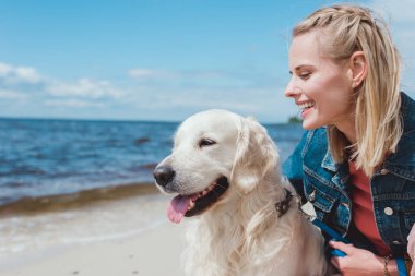 Golden retriever köpek ile deniz kıyısında oturan güzel gülümseyen kadın