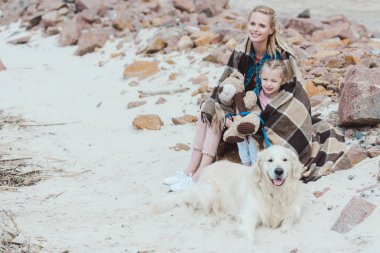 Anne ve kızı ile golden retriever kıyıda oturan battaniyeye