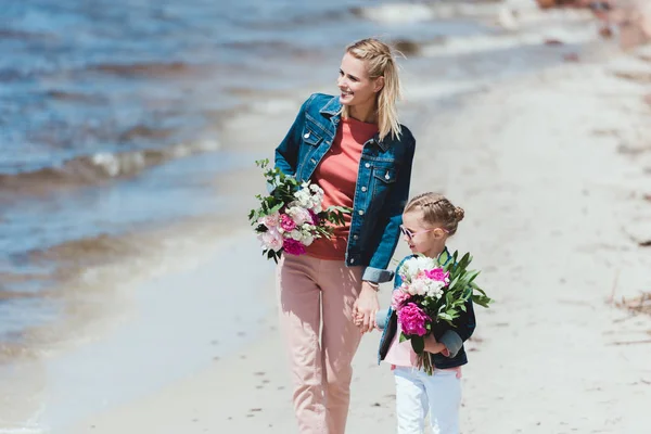 有吸引力的母亲和女儿与花束牵手在海岸边 — 图库照片