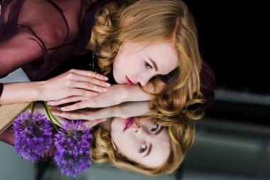 Genç kadın ile mavi çiçekler ayna üzerinde yatarken yansıma bakarak 