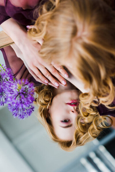 selective focus of young woman looking at reflection while lying on mirror with blue flowers  