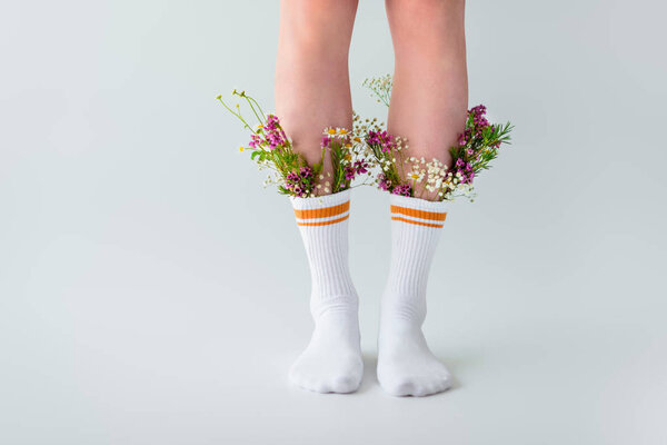 cropped shot of girl in socks with fresh flowers isolated on grey  