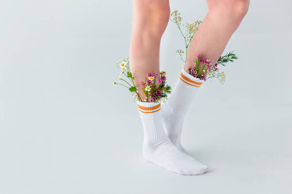 частичный вид молодой женщины в носках с красивыми свежими цветами, изолированными на сером
  