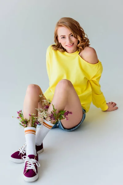 靴下に座って グレーに分離カメラで笑顔の花で美しい少女 — ストック写真