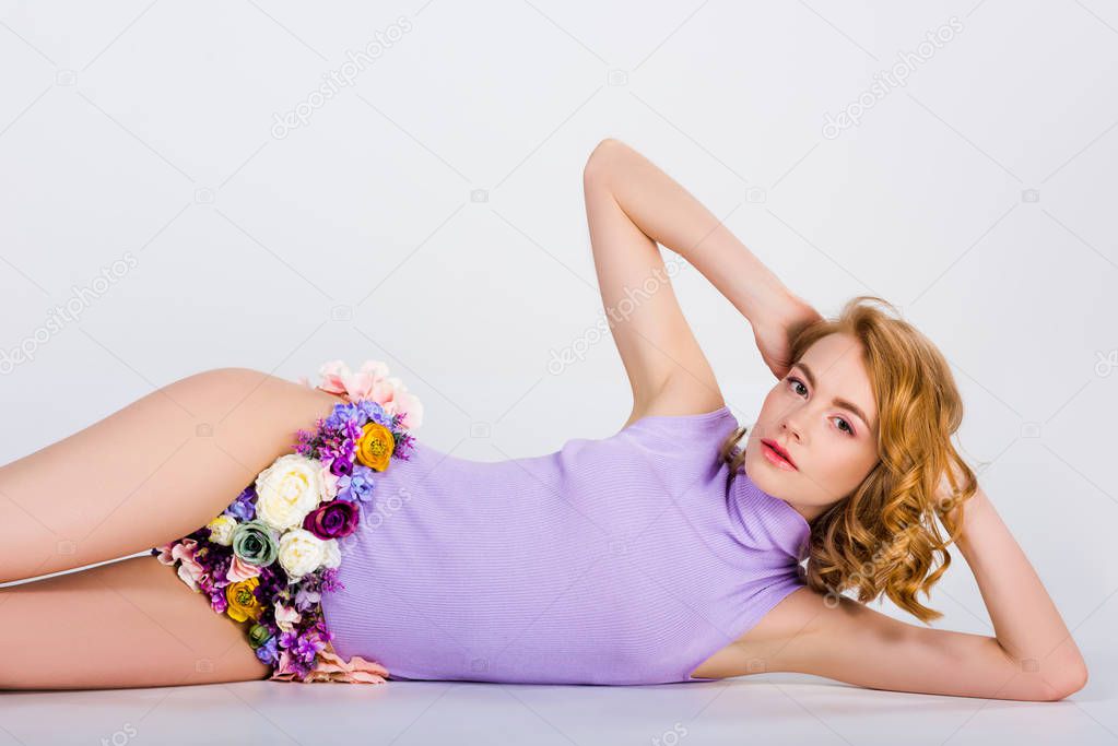 beautiful tender girl in panties made of flowers lying and looking at camera on grey