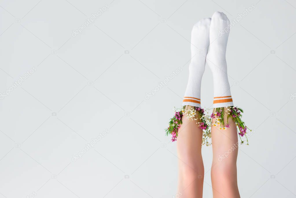 upside down view of female legs with fresh flowers in socks isolated on grey 