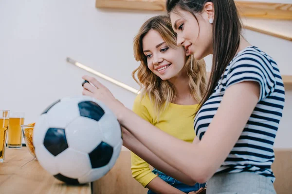 Zijaanzicht Van Twee Glimlachend Vriendinnen Kijken Voetbalwedstrijd Toog Met Voetbal — Stockfoto