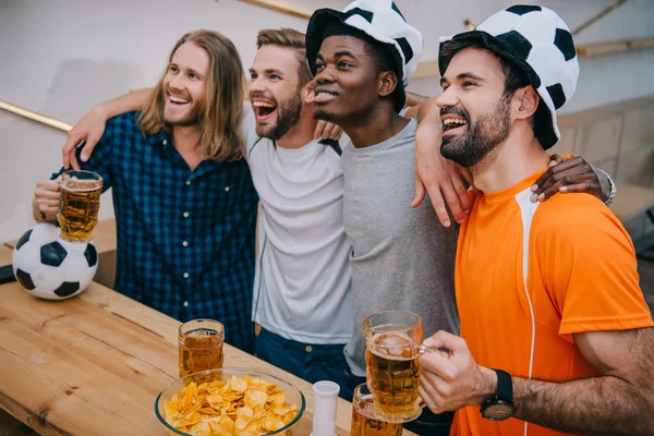 ビールを押しながらサッカーの試合を見てサッカー ボール帽子の男性サッカーファンの興奮している多文化グループ — ストック写真
