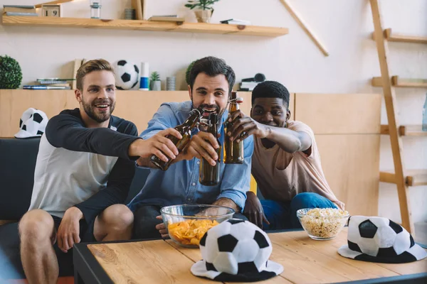 微笑的年轻多元文化的朋友无比的啤酒瓶和庆祝在观看足球比赛在家里 — 免费的图库照片