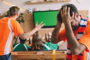 hayal kırıklığına uğramış genç adam Turuncu tişört ve elele arkadaşları evde tv ekranında maç futbol izlerken ederken kafasına eşarp 