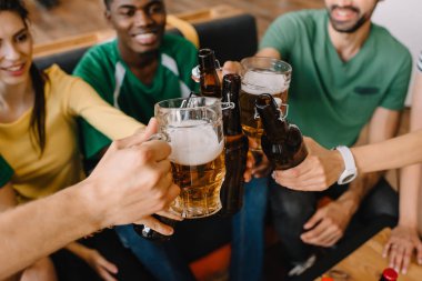 closeup view of multicultural football fans celebrating and clinking beer bottles and glasses  clipart