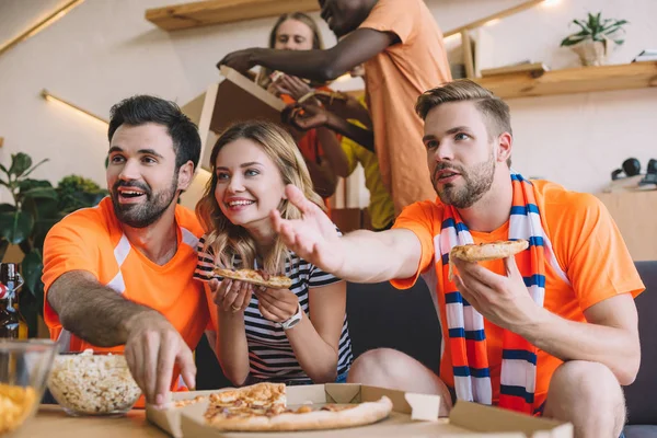 Giovane Indicando Mano Suoi Amici Mangiare Pizza Guardare Partita Calcio — Foto Stock