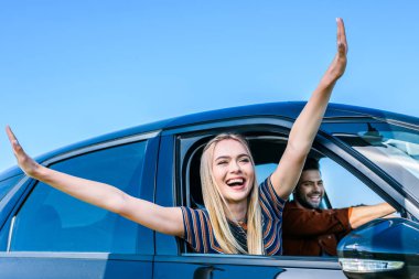 happy young woman with wide arms leaning out from car window while her boyfriend driving car  clipart