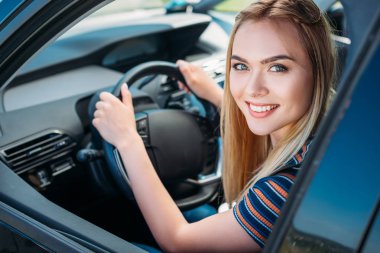 arabanın direksiyonuna oturan gülümseyen genç kadın portresi 