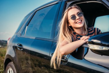 happy stylish woman in sunglasses leaning out from car window  clipart