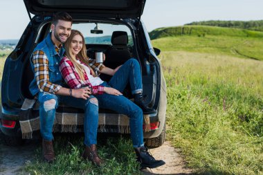 kırsal alan araba bagajında oturup kahve fincanı ile gülümseyen çift 