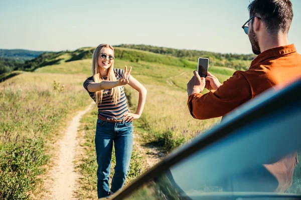 Man Nemen Foto Van Vriendin Doen Vredesteken Buurt Van Auto — Stockfoto