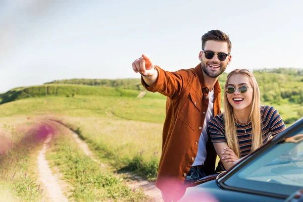 Jovem Homem Elegante Apontando Mão Para Mulher Sorridente Perto Carro — Fotografia de Stock