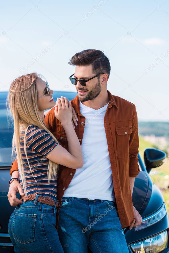 smiling stylish couple in sunglasses standing near car 