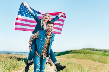 Genç adam Amerikan bayrağı kırsal çayır, bağımsızlık günü kavramı üzerinde tutan kız için Atçılık yapıyor