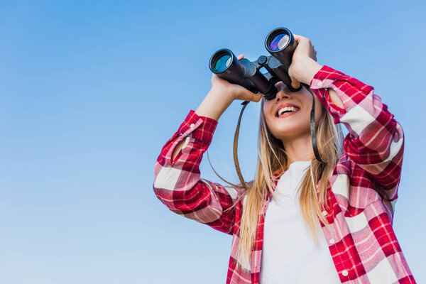 low angle view of female traveler looking through binoculars against blue sky