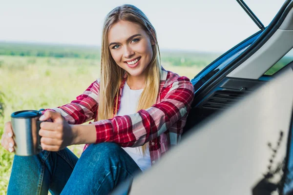 Glimlachend Jonge Vrouw Zittend Auto Kofferbak Met Koffiekopje Landelijk Gebied — Stockfoto