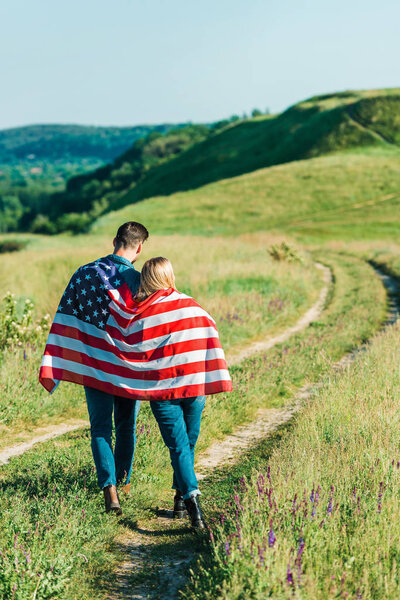 вид сзади на молодую пару с американским флагом на сельском лугу, концепция Дня независимости
