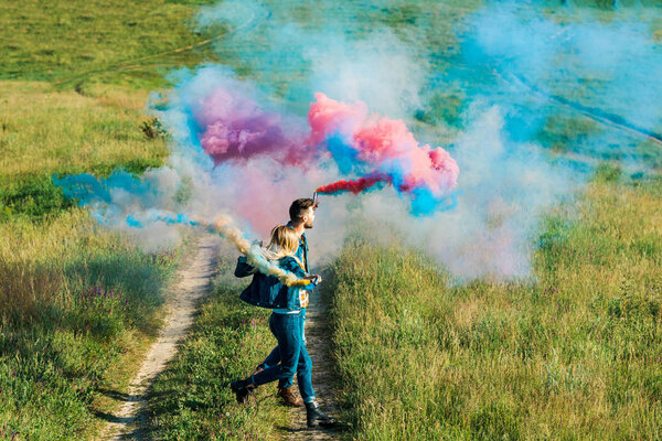 side view of couple holding colorful smoke bombs in field