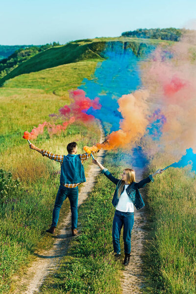  view from above of young couple holding colorful smoke bombs on rural meadow 