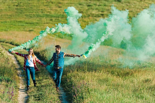 在农村草地上持有绿色烟雾弹的年轻夫妇的正面看法 — 图库照片