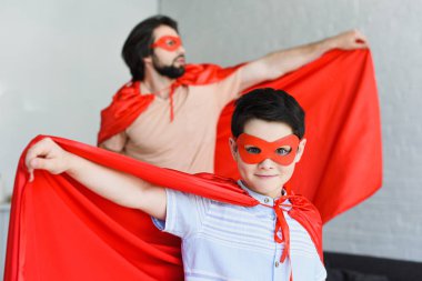 seçici odak küçük oğul ve baba evde kırmızı süper kahraman kostümleri