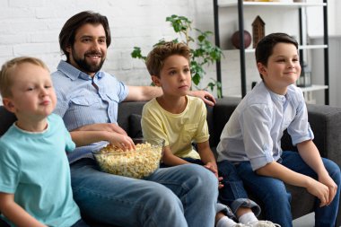 adam ve küçük oğulları birlikte evde film izlerken patlamış mısır ile gülümseyen