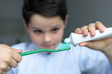 selective focus of little boy putting tooth paste on tooth brush in hand at home clipart