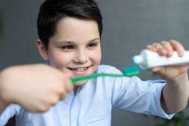 selective focus of little boy putting tooth paste on tooth brush in hand at home clipart