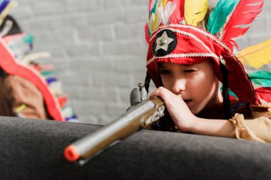 little boy in indigenous costume with toy gun playing at home clipart