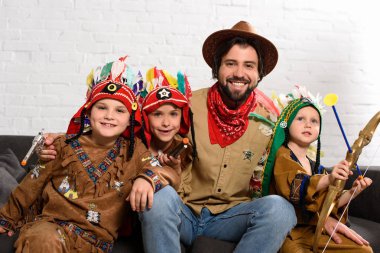 şapka ve küçük oğlu evde yerli kostümleri ile kanepede oturan kırmızı bandana gülümseyen baba