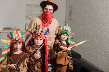 küçük çocuklar yerli kostümleri ve babası evde kameraya seyir şapka ve kırmızı bandana portresi