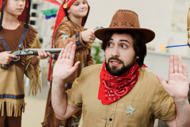 father in hat and bandana and little sons in indigenous costumes with toys playing together at home clipart