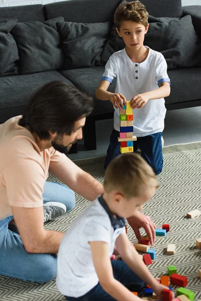 父亲和孩子们一起在地板上玩木块的侧面视图 — 图库照片