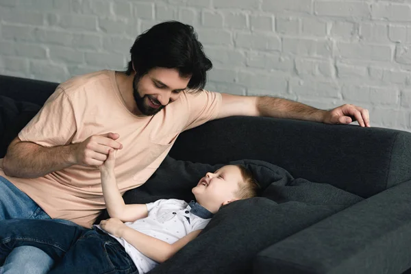 幸せな父と幼い息子の自宅のソファの上で一緒に楽しんで — ストック写真