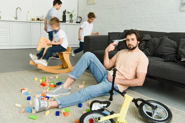 床と部屋で遊んで子供の上に座って頭におもちゃの銃で疲れた男 — ストック写真