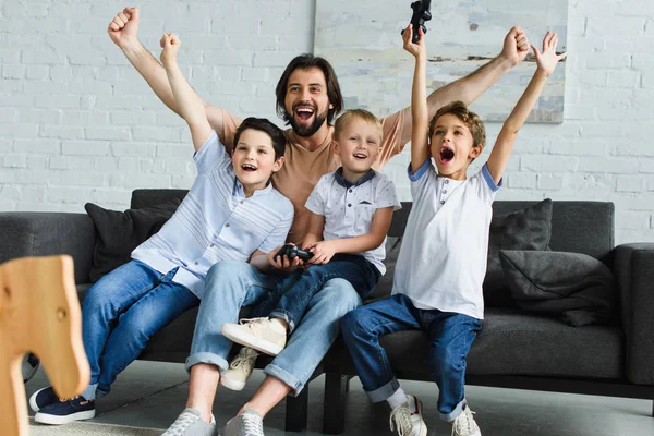 Feliz Padre Hijos Pequeños Sentados Sofá Jugando Videojuegos Juntos Casa —  Fotos de Stock